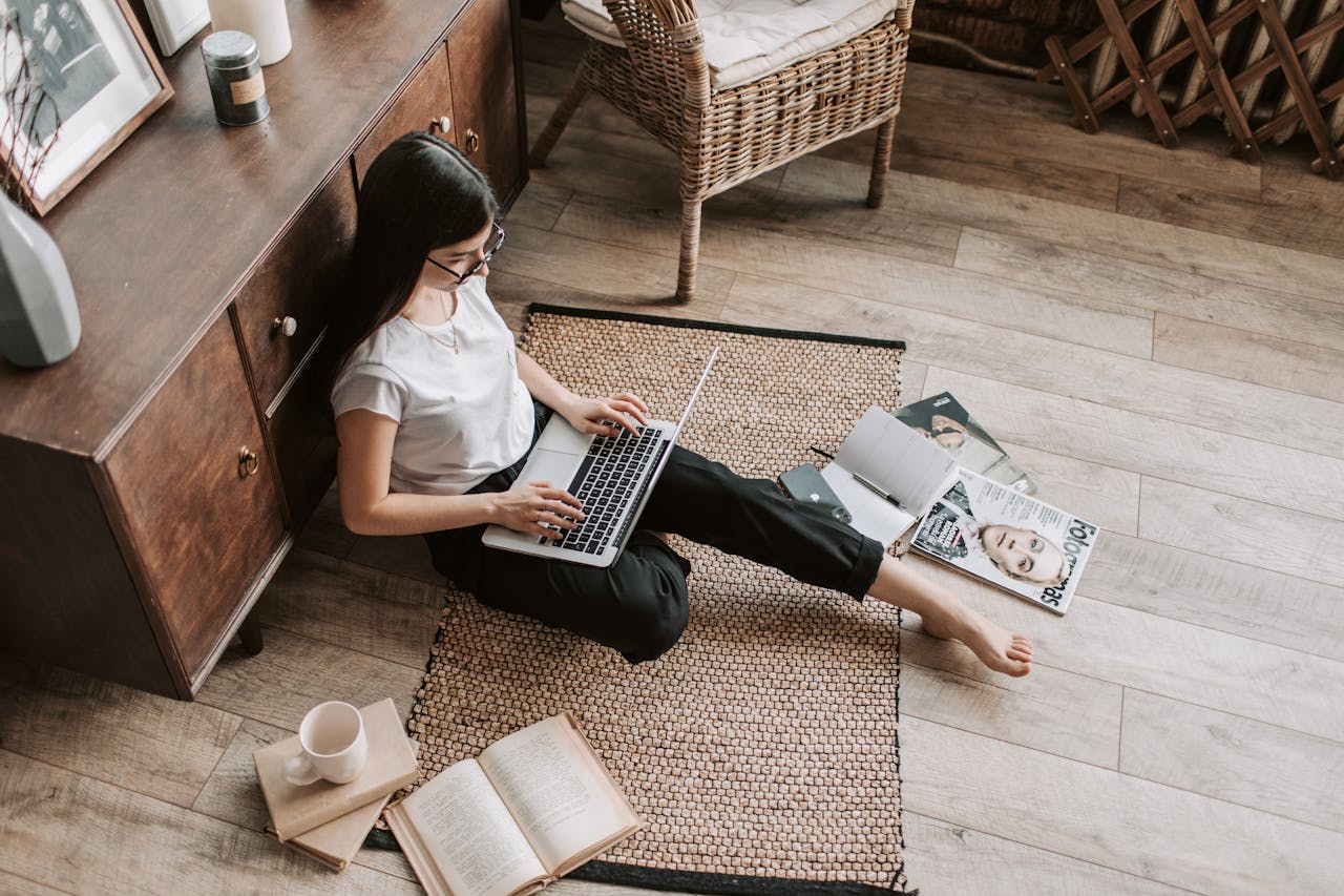 Casual home workspace with a woman using a laptop, surrounded by books and magazines.